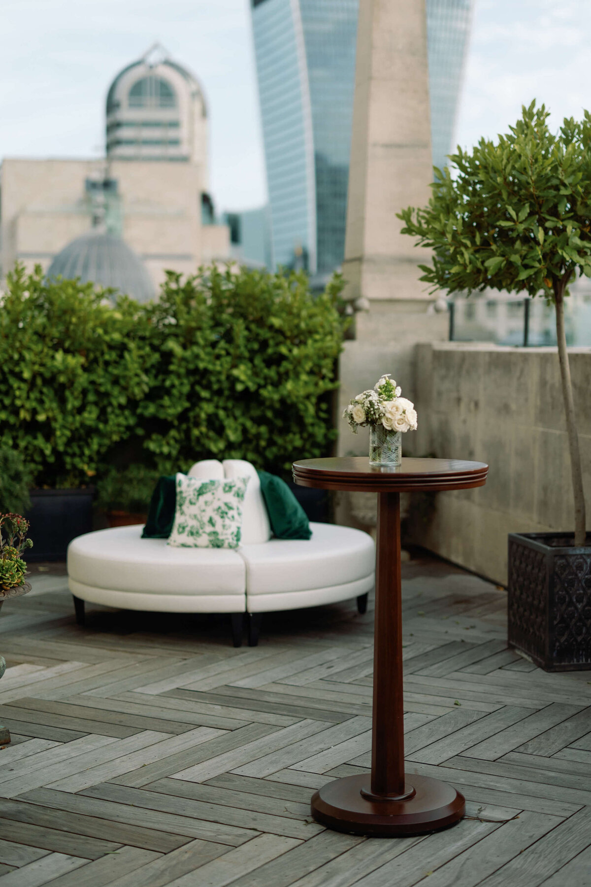 the rooftop of the ned hotel set up for a chic wedding drinks reception with white sofa and green cushions with the the london skyline behind it