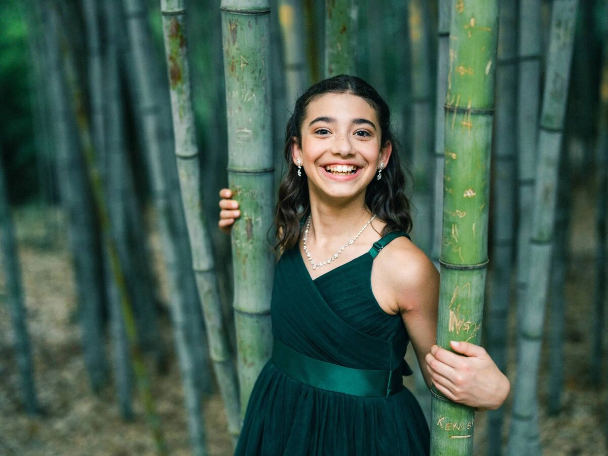 A teenager holding onto bamboo trees and smiling.