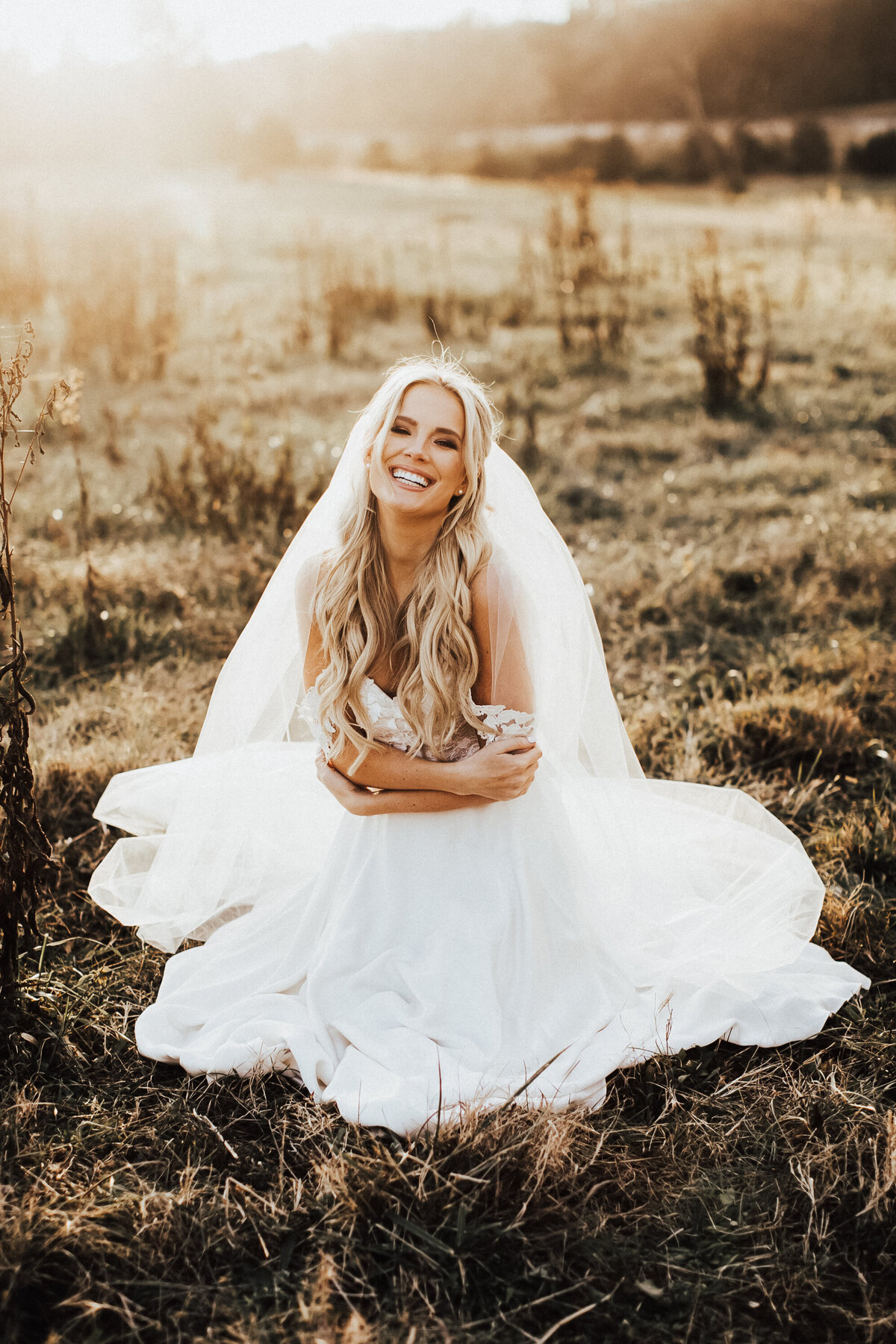 bride in her dress sitting in a field at golden hour