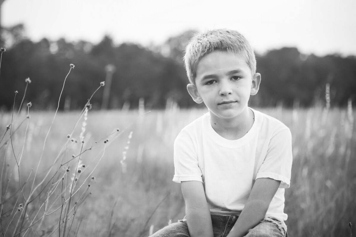 black-and-white-photograph-of-boy-in-white-shirt-sitting-on-stool-in-field