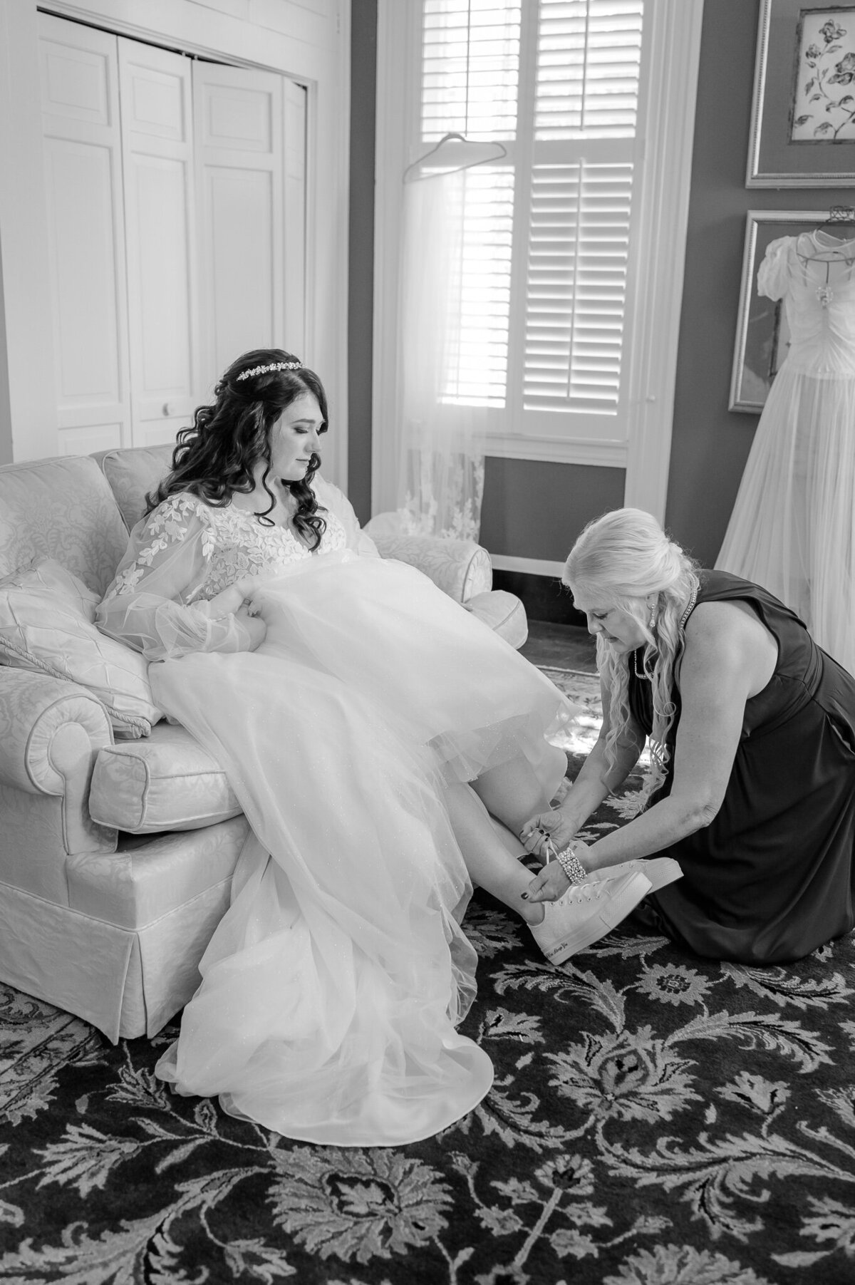 A mom helping her daughter put on her wedding shoes on her wedding day while enjoying their Raleigh wedding photos