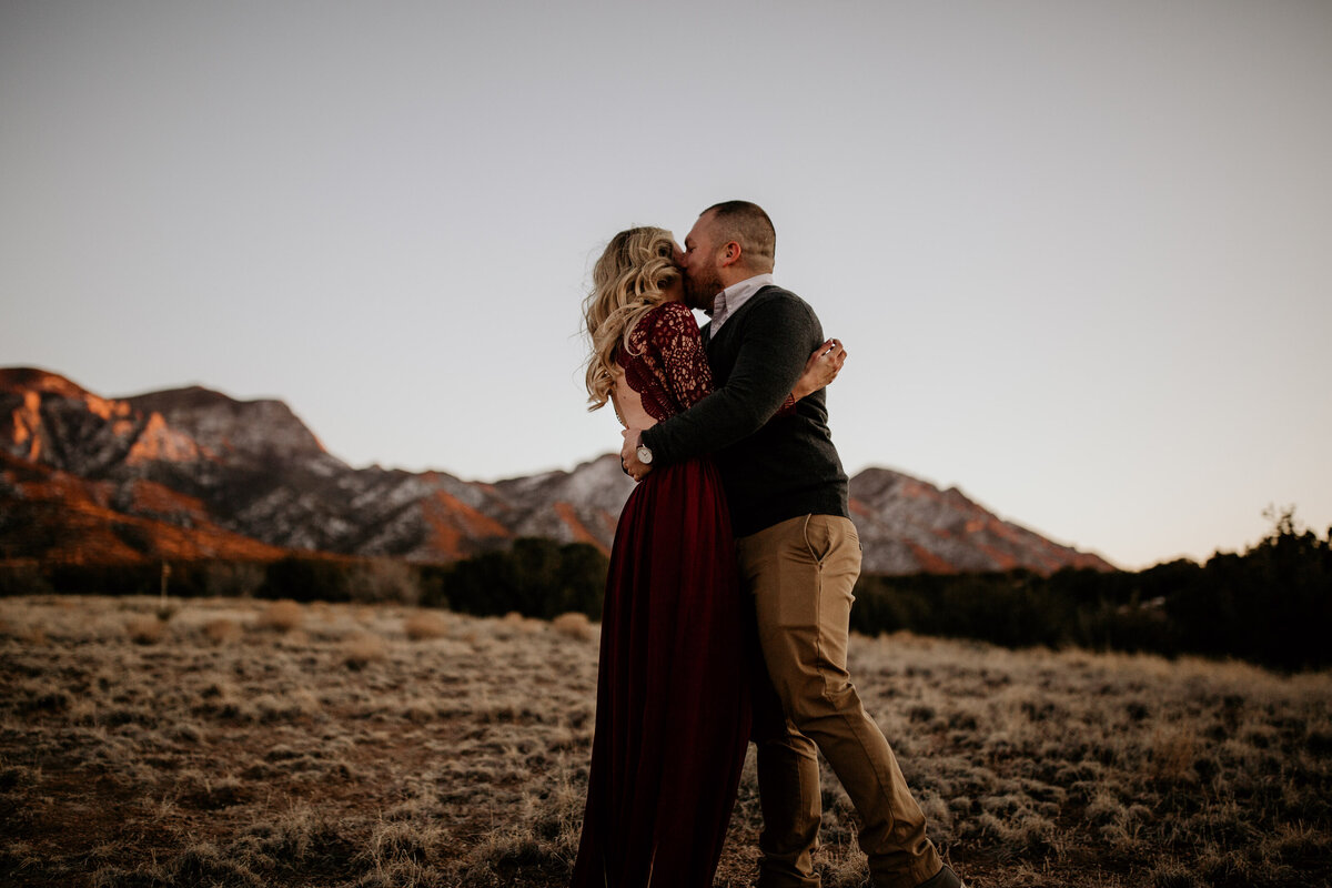 Engaged couple kissing in the Albuquerque desert with the mountain behind them