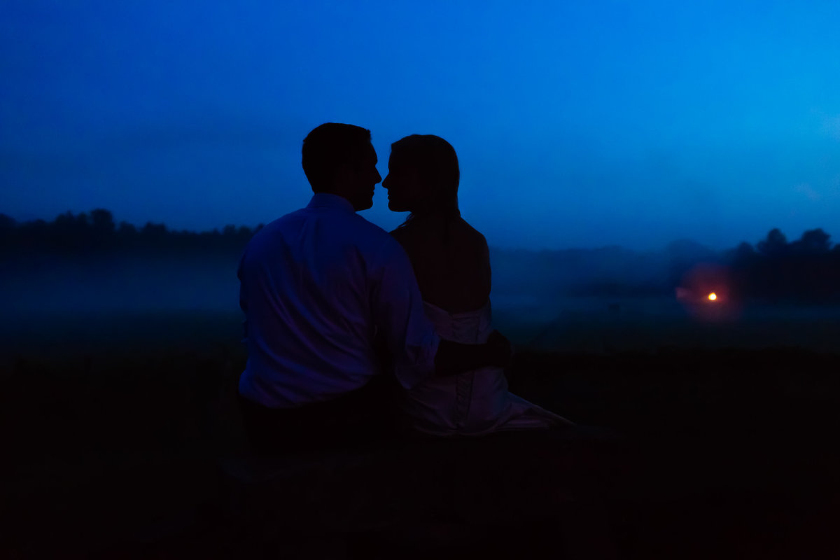 A blue hour silhouette of the bride and groom with mist and a bonfire in the distance at Flag Hill Winery NH