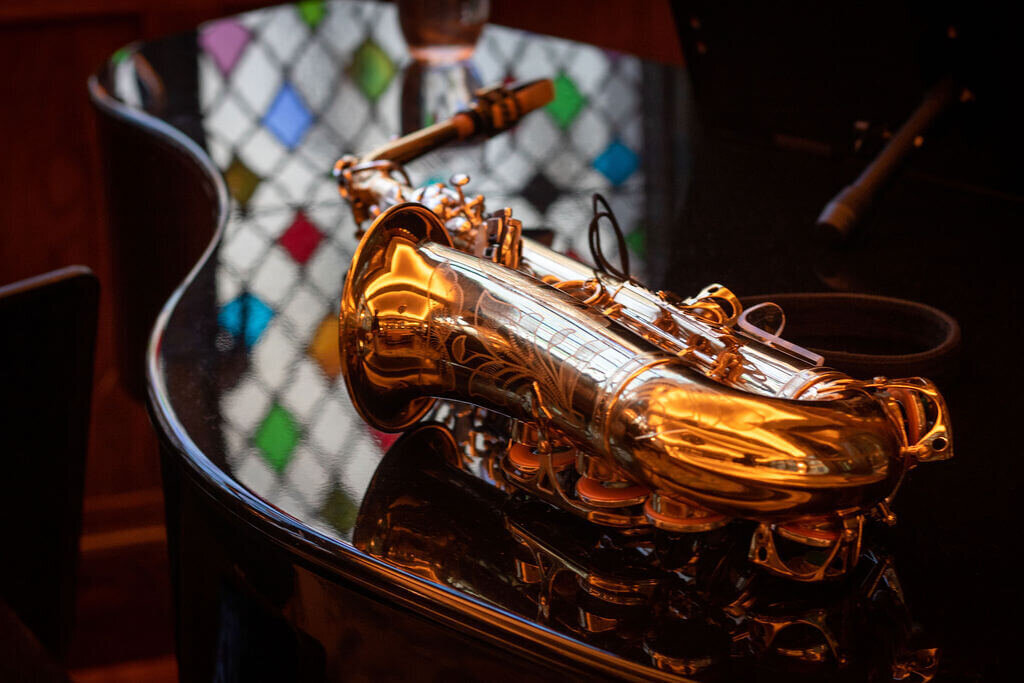 Gold saxophone lays on top of piano.  Instruments are very shiny