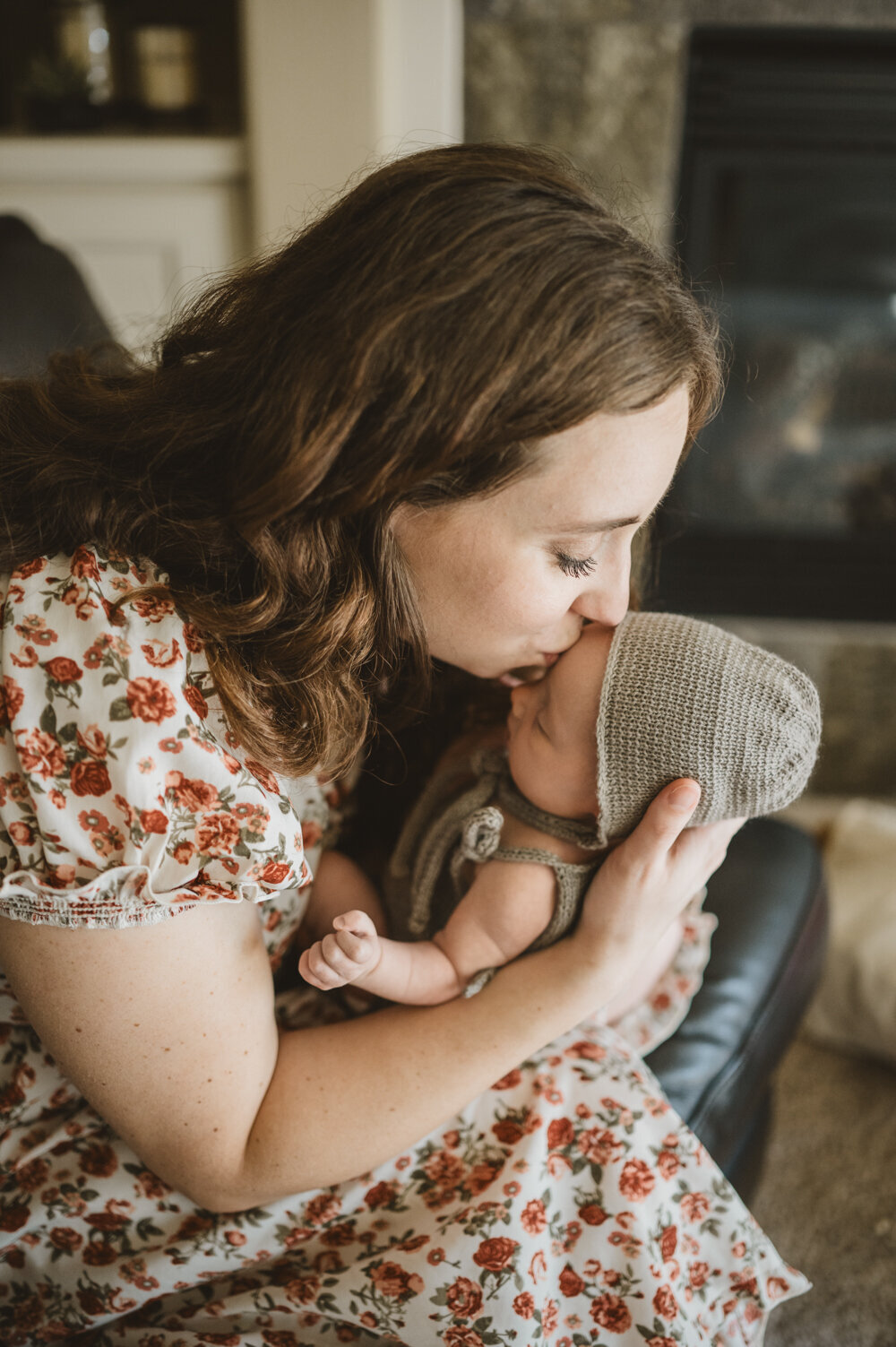 Mother kissing newborn wearing a knit bonnet, capturing a tender moment of early bonding during a cozy in-home newborn session in Portland.