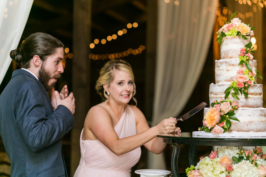 Bridesmaid pretends to cut the wedding cake as the groomsman looks on pretending to be shocked.
