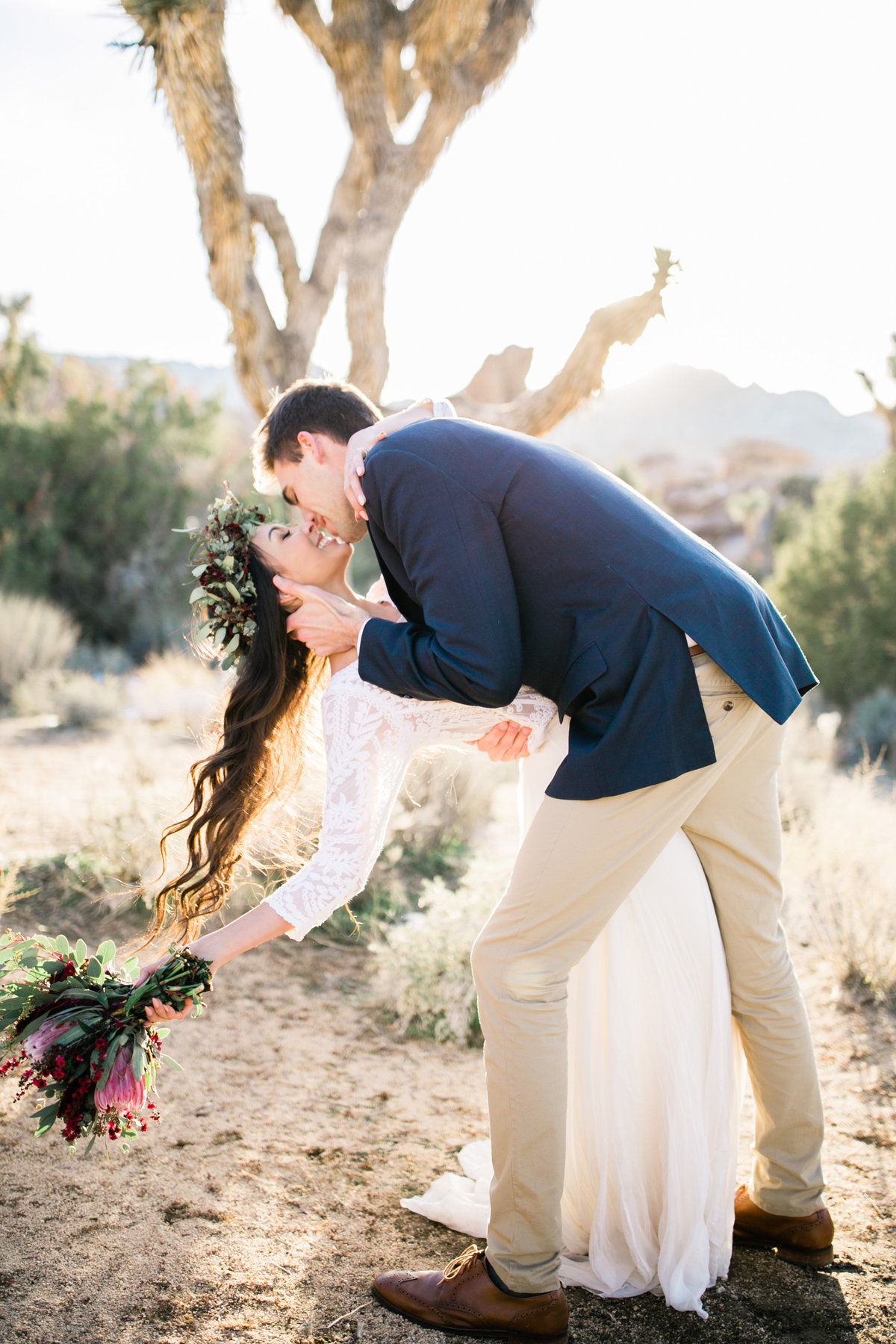 the groom dips his bride into a kiss in front of a joshua tree during their elopement