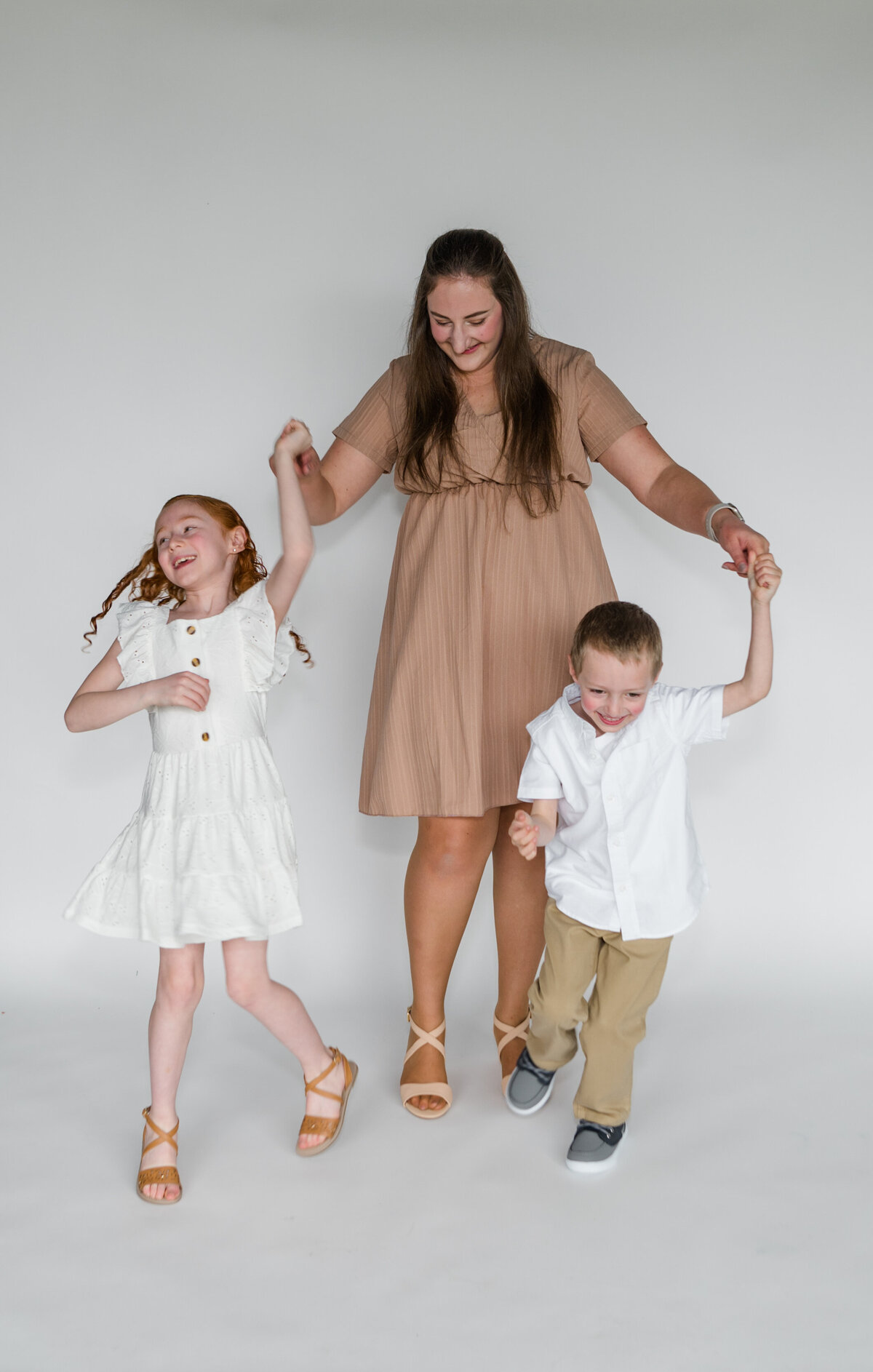 Mothers day mini in a studio, mom looks at her kids as they spin around in a circle laughing.