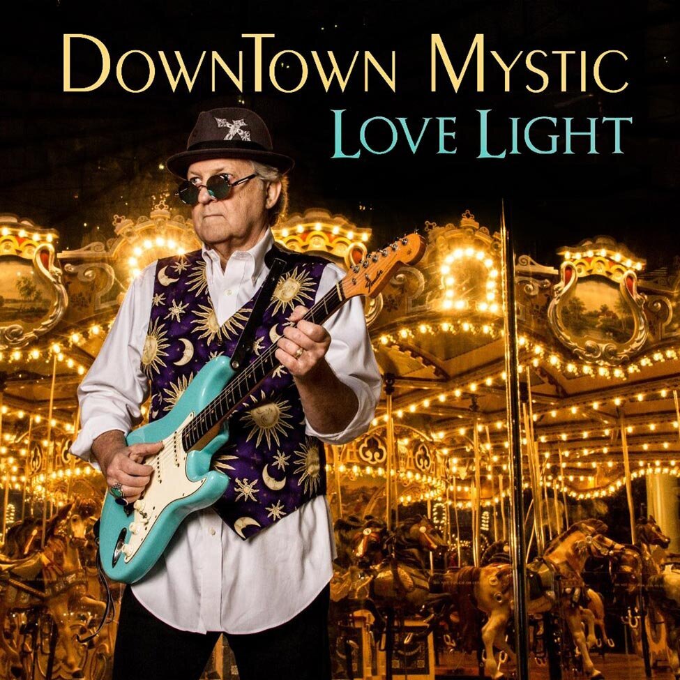 Single Cover Artist Downtown Mystic title Love Light Singer standing in front of lighted carousel strumming blue electric guitar