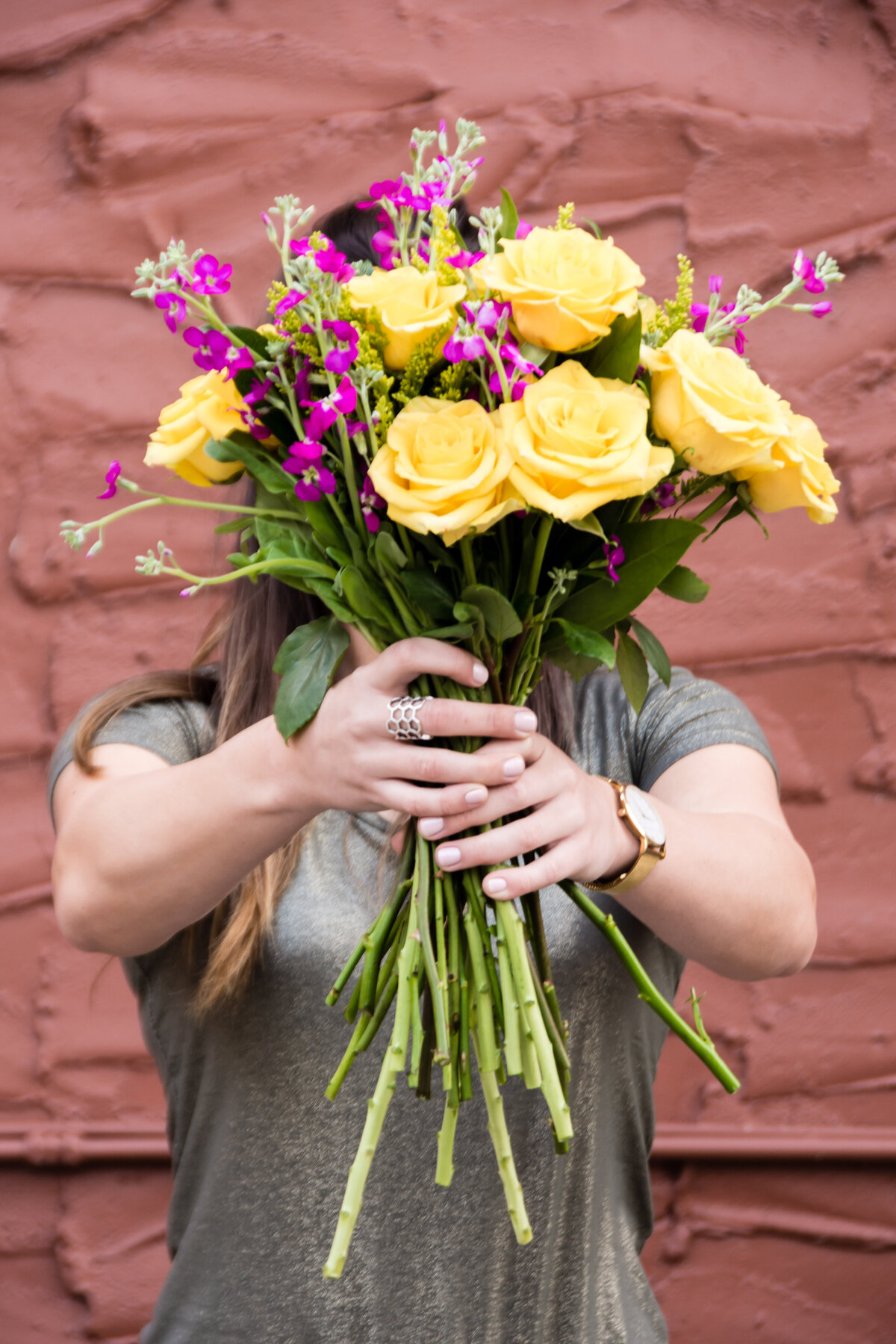 Woman holds bouquet of yellow and pink flowers up in front of her face