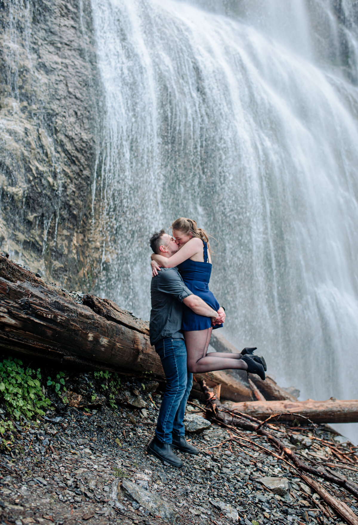 Guy picks up girl and girls legs out and couple kisses by the bridal veil falls.