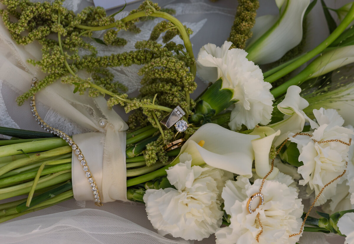 wedding details of wedding rings, white and green bouquet on a wedding dress.