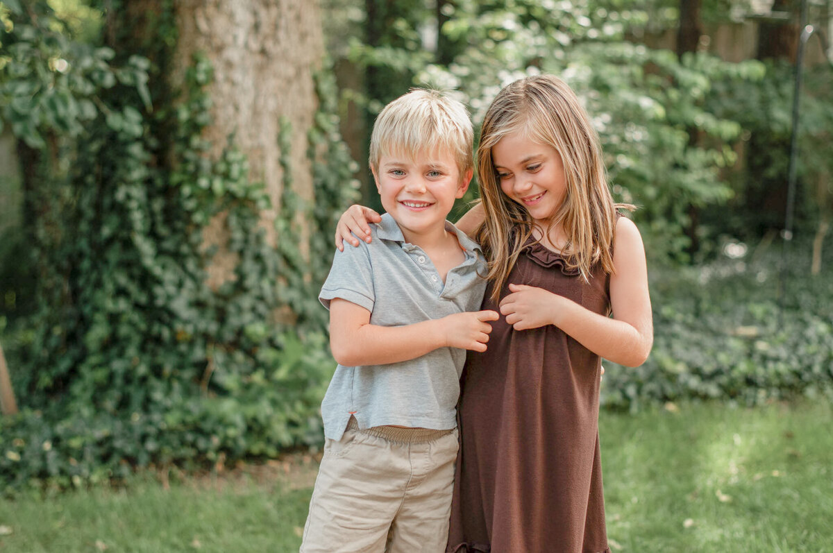 Brother and sister stand with their arms around each other and laugh together during pictures.