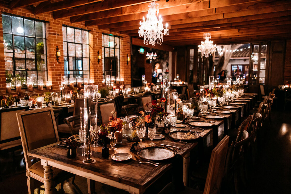 Indoor wedding reception set up in a moody historic house featuring dimmed lightning, long wooden tables, and tall glass vases.