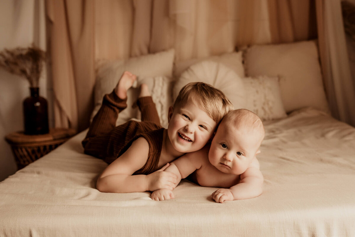 Brothers smiling and snuggling on a bed.