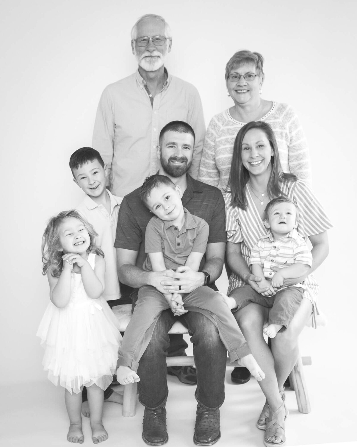 family of 5 and grandparents in studio for a family portrait.  Kids looking so adorable, edited in light and airy black and white