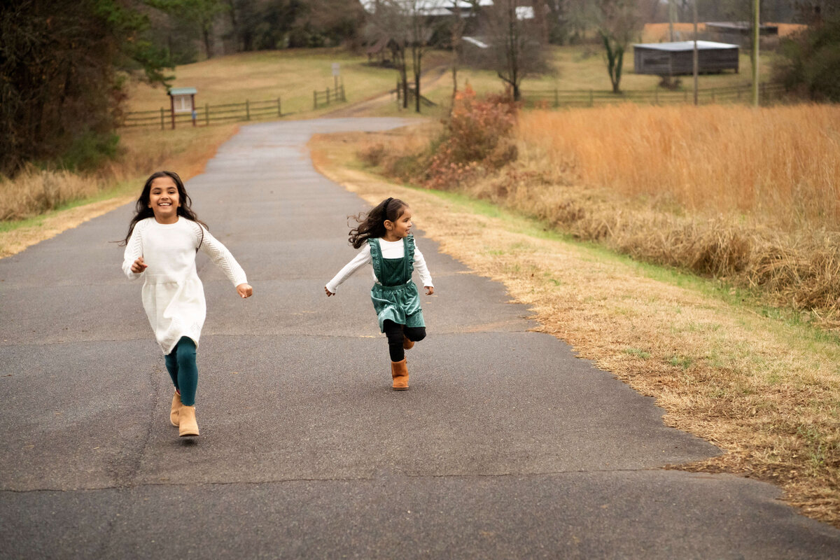 Two young girls running down paved road next to a field by Atlanta family photographer