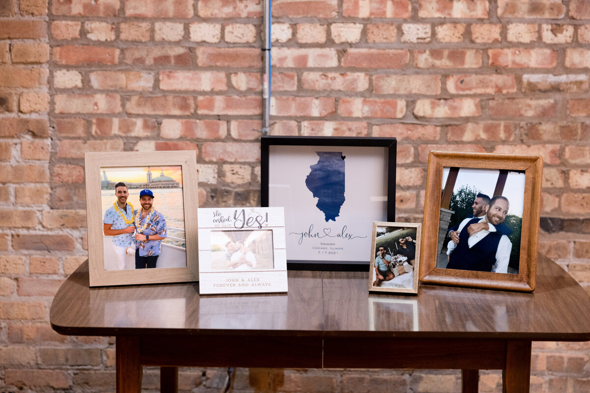 Five picture frames sit on a wooden table in front of a brick wall at Chicago LGBTQIA+ wedding.