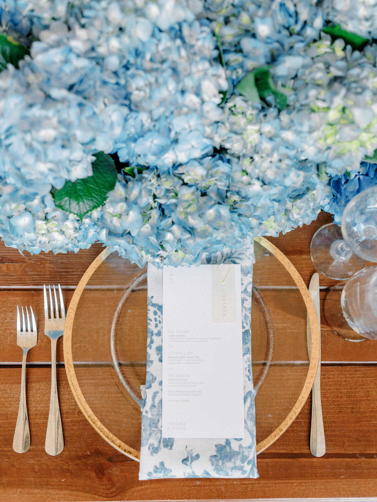 Reception table setting with clear plate, blue and white floral napkin, and blue hydrangea centerpiece