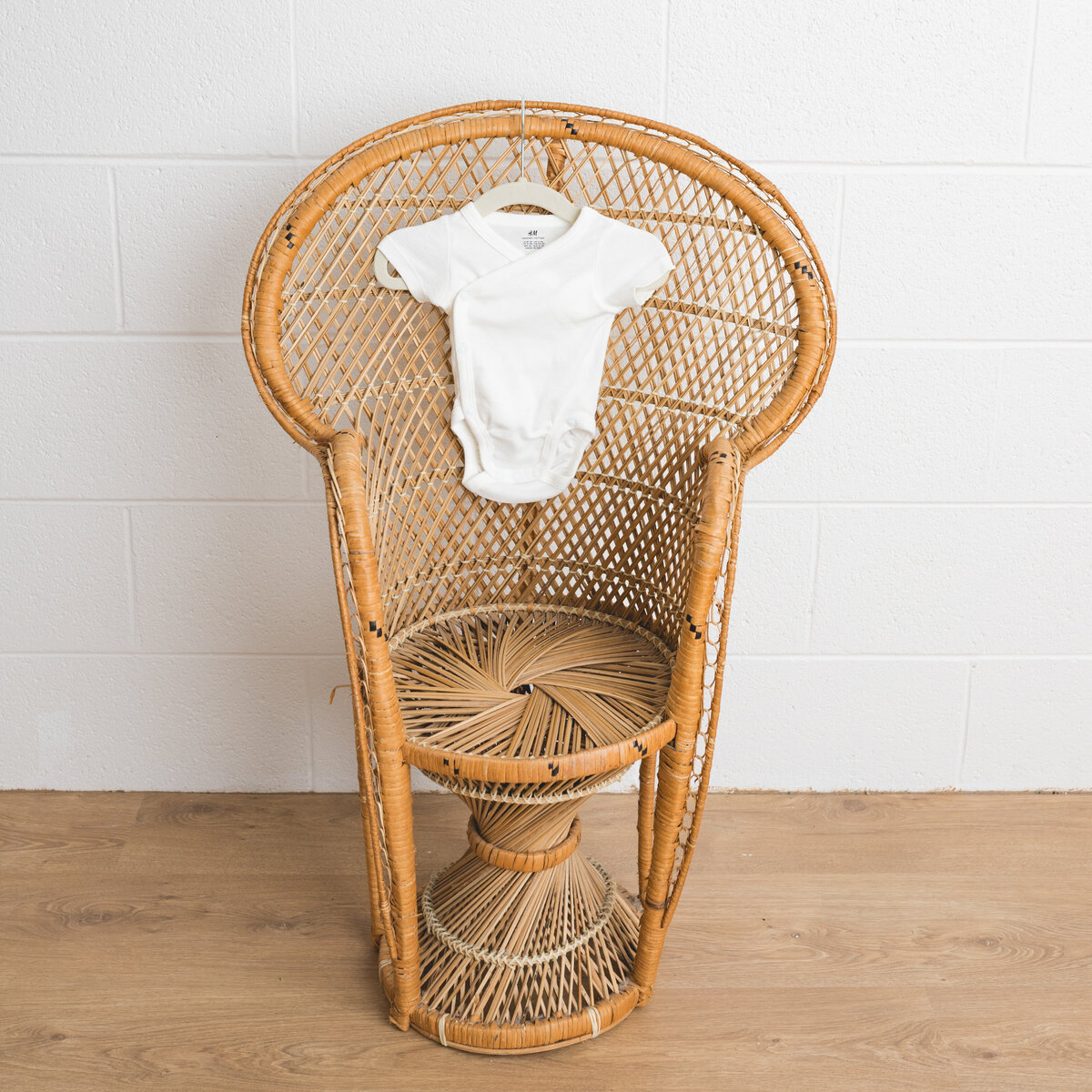Image depicts a miniature peacock chair in a photography studio on the chair hangs a tiny newborn outfit in white knit .  This image is a sample of Lauren Vanier Photography's newborn client wardrobe. Image taken in Hobart Tasmania