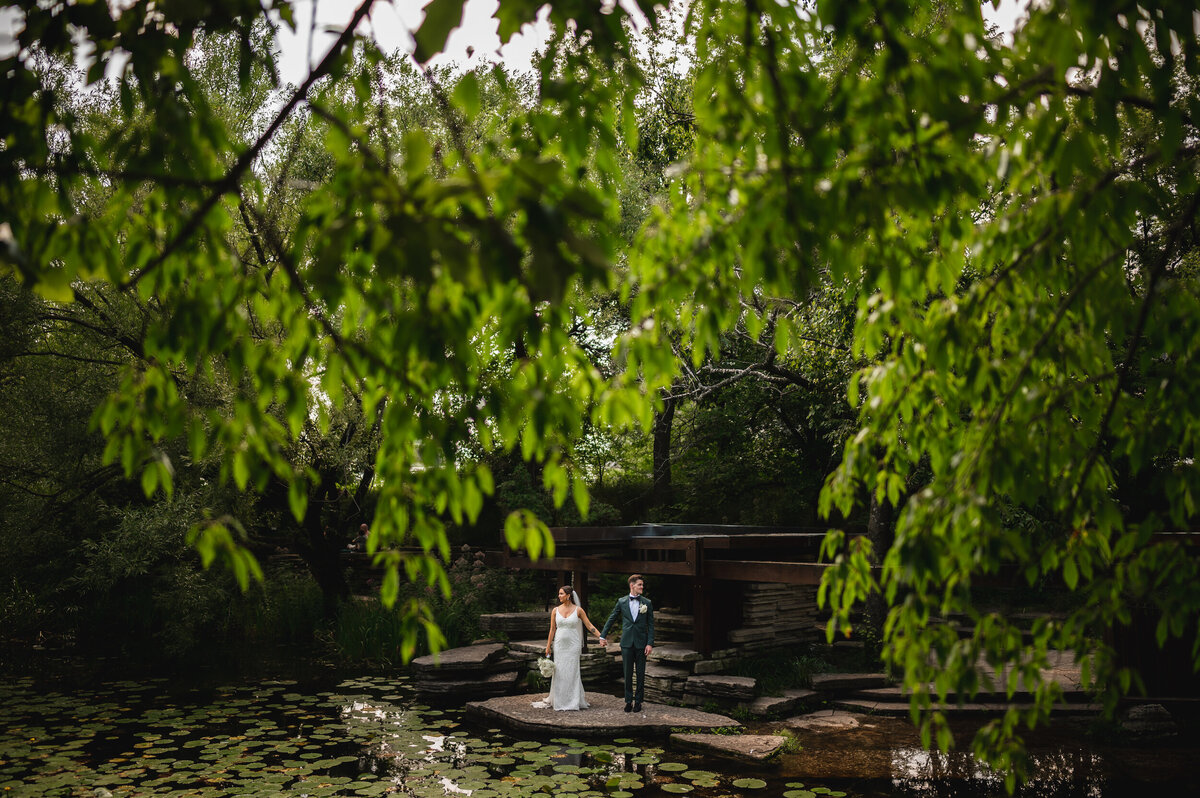 Bride and groom stand next to the water at Alfred Caldwell Lily Pool in Chicago, Illinois