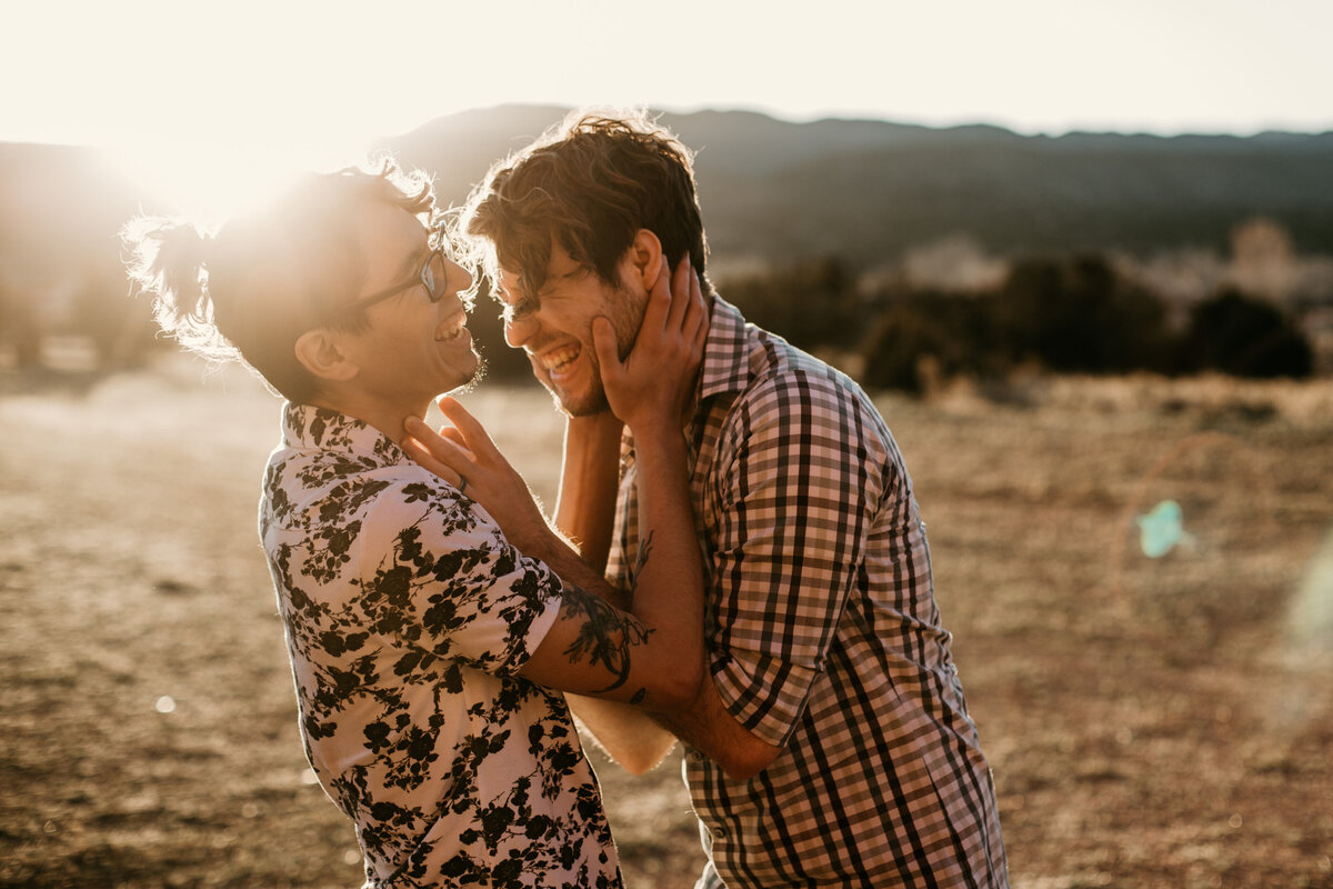 same sex couple holding each others faces with sun flare