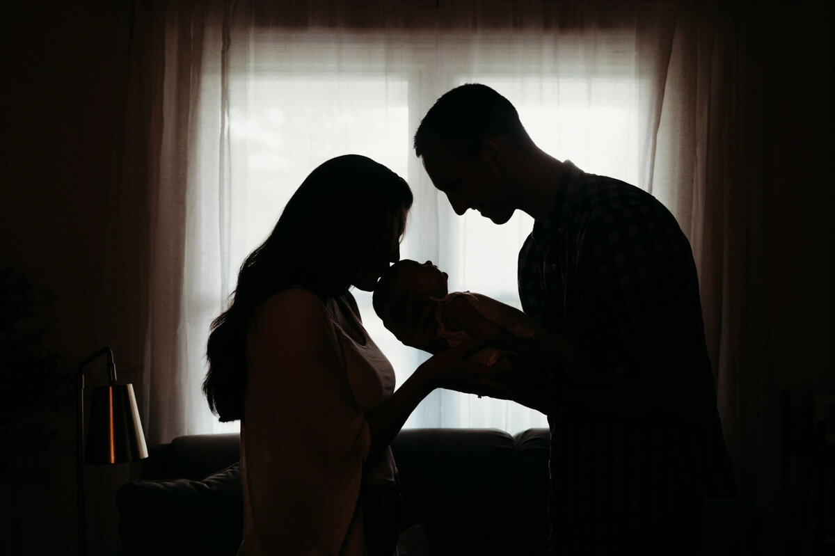 silhouette of dad holding baby and mom kissing baby's head