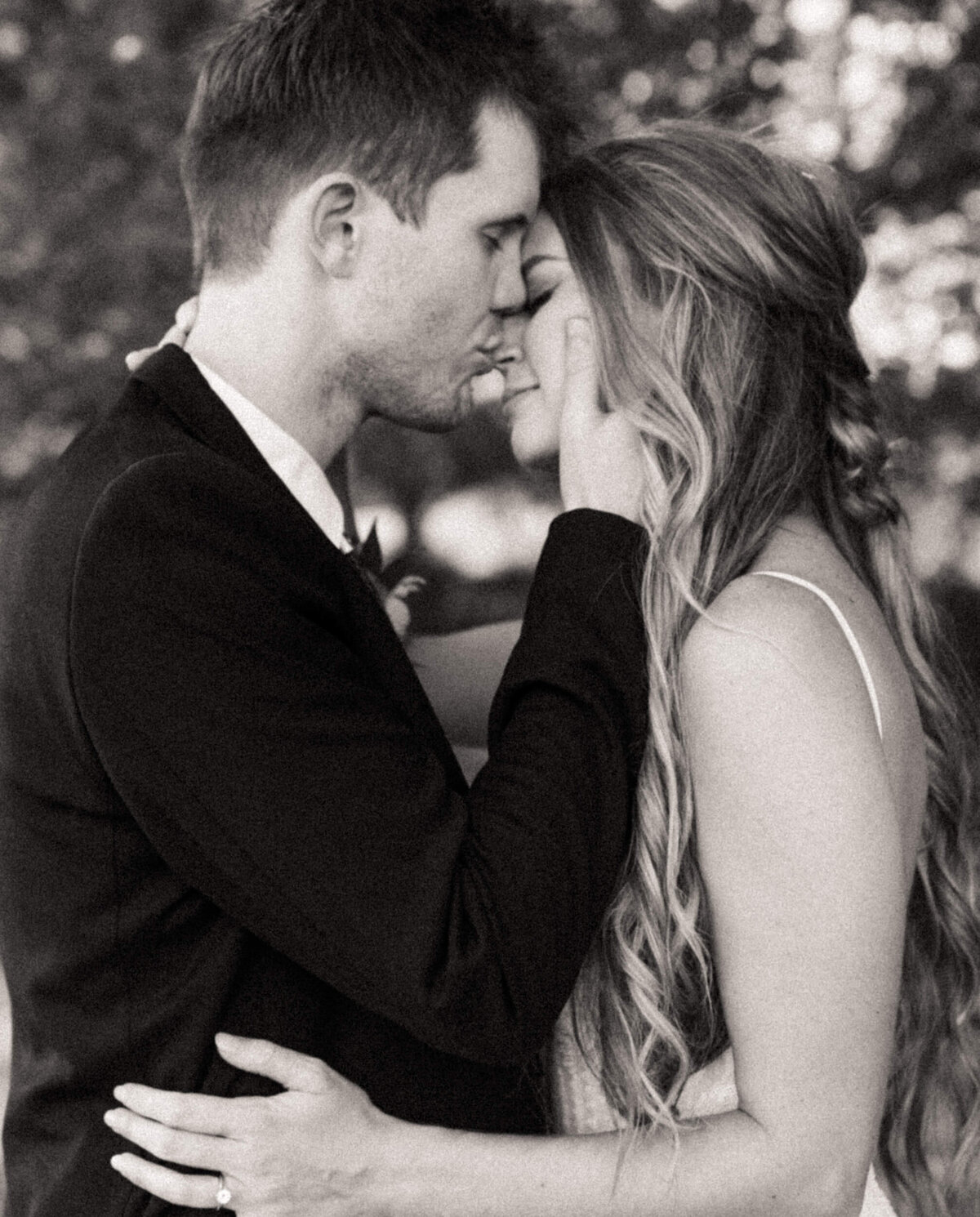 Bride with long loose curls smiling and closing her eyes as her groom kisses her nose