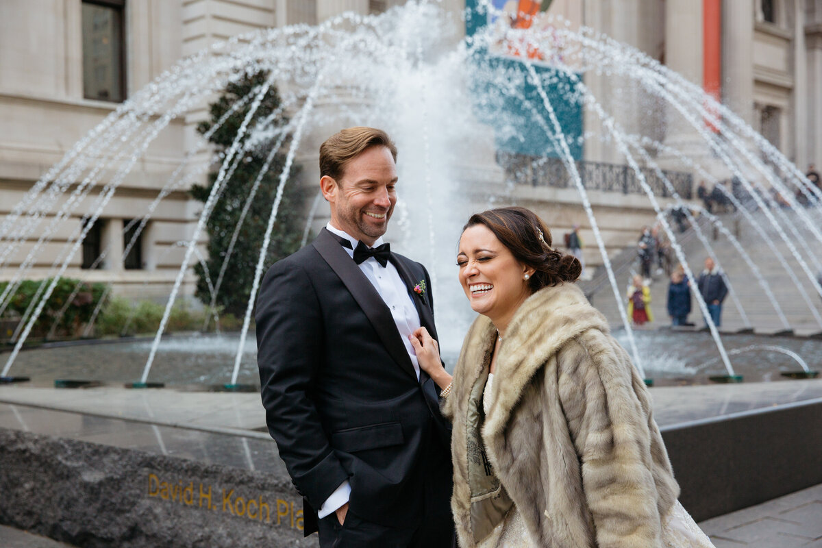 A couple laughing while standing in front of a water fountain.