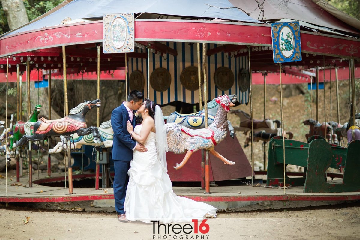 Groom shares a kiss with his Bride in front of a carousel at Calamigos Ranch