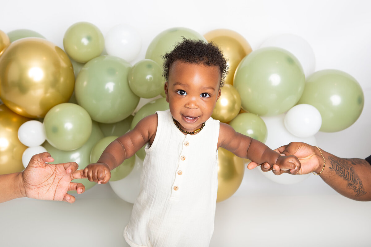 Baby infront of a white gold and olive balloon garland