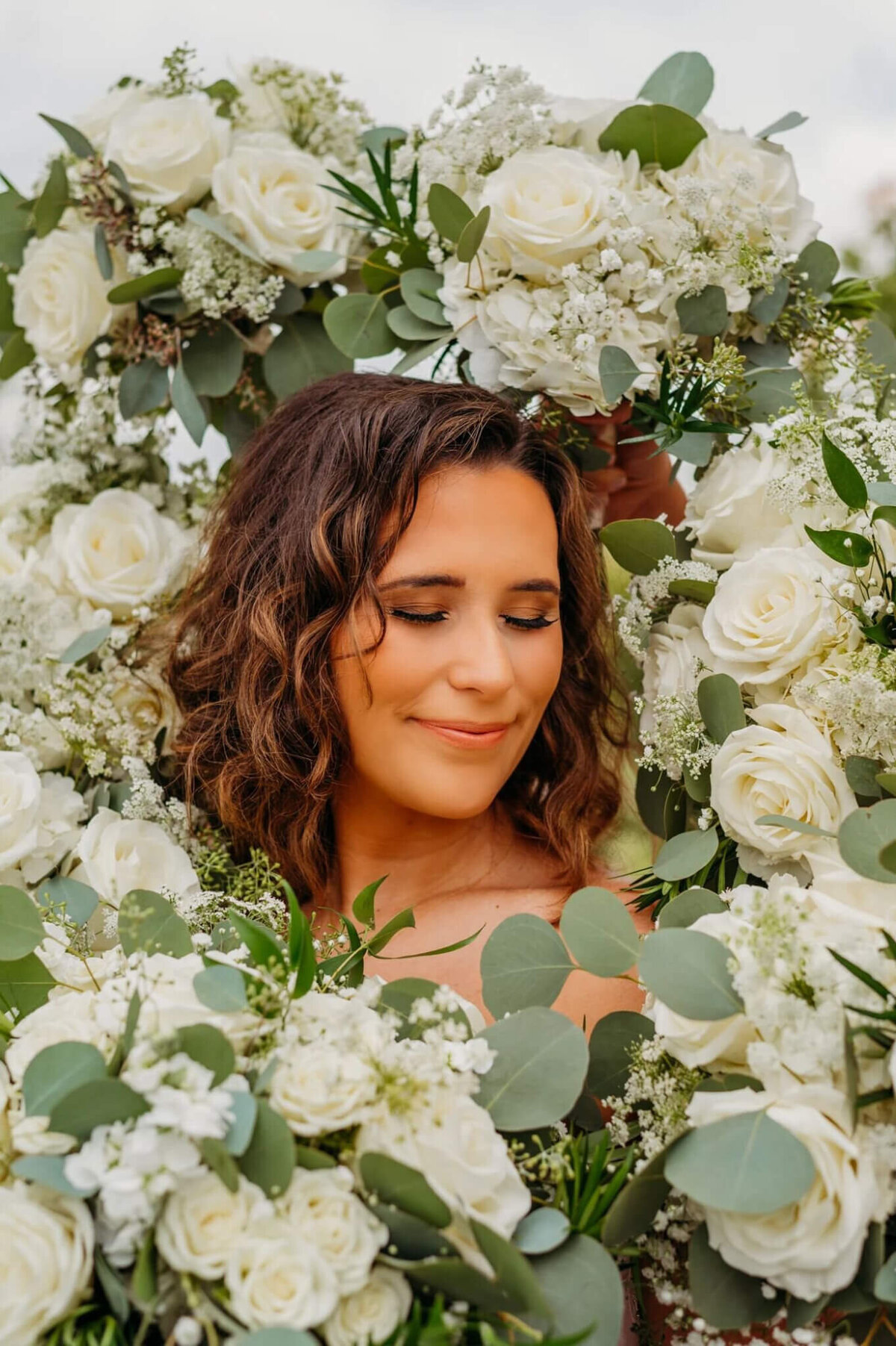 Photo of a woman smiling and closing her eyes popping surrounded by white florals and greenery