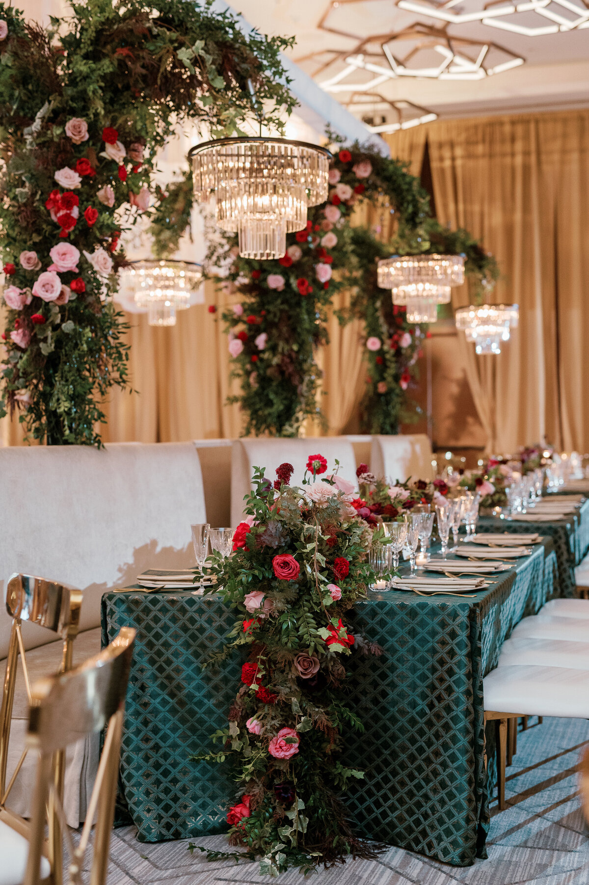 Standing chandeliers covered in lush florals for winter wedding at the Four Seasons. Jewel tone wedding reception florals with reception table floral cascades. Winter floral colors in ruby, blush, plum, and magenta. Design by Rosemary & Finch Floral Design.
