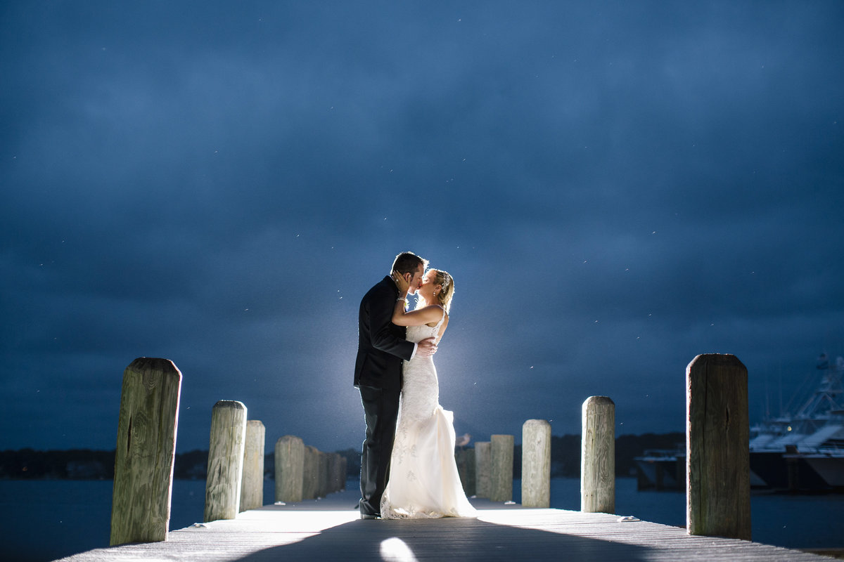bride and groom kissing on dock at night at clarks landing yacht club wedding