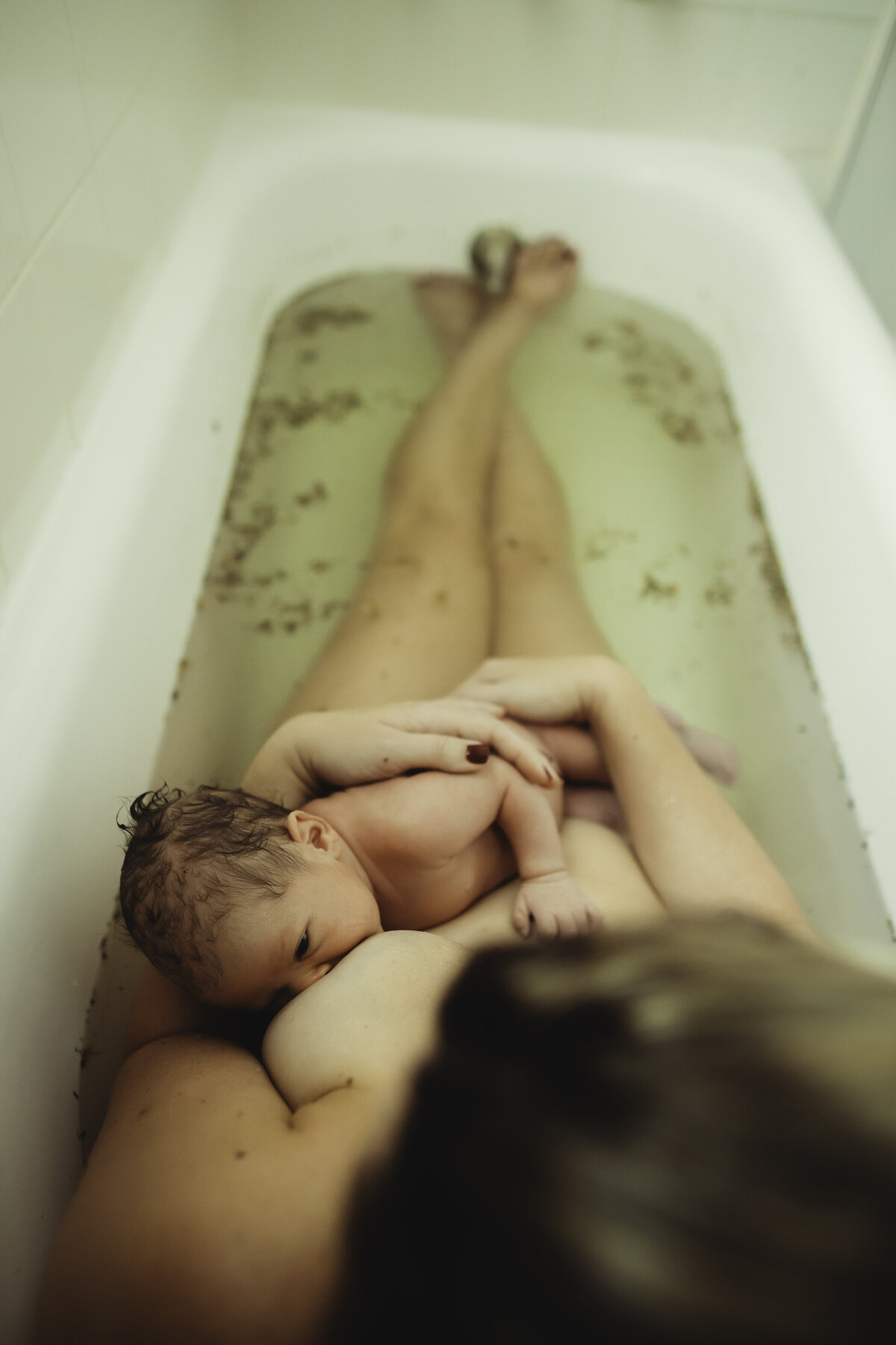 a mom breastfeeding her newborn in a herbal bath during a photo session at home