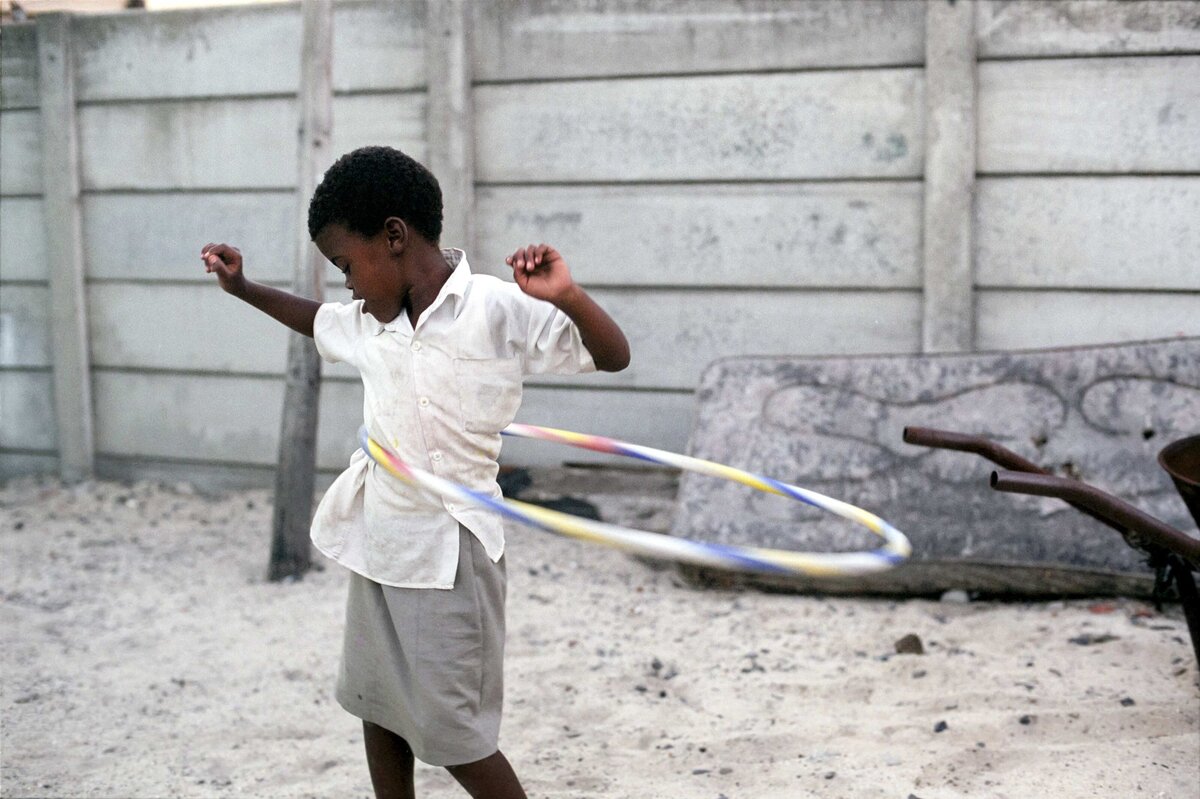 A young girl hula hoops with of mattress in background. An editorial photo showing resilience of a historially marginalized group of people.