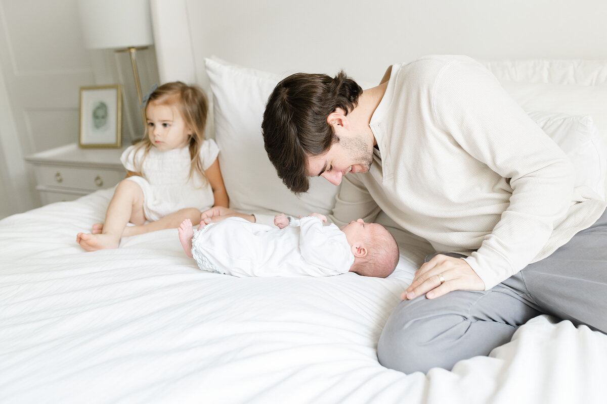 a father connecting with his newvborn baby on a white bed