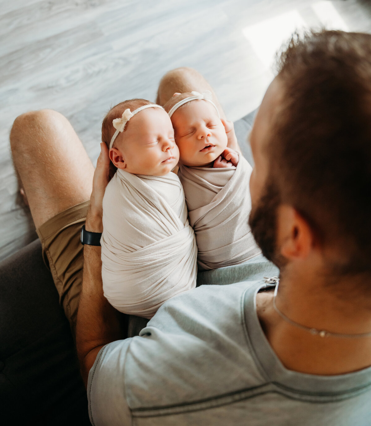 Newborn Photographer, a father sits holding his twin baby girls in his lap