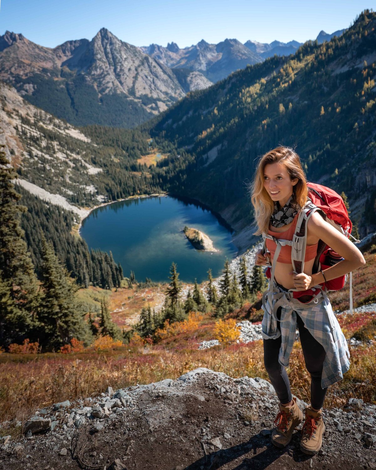 Woman with a red backpack standing on a mountain above a lake