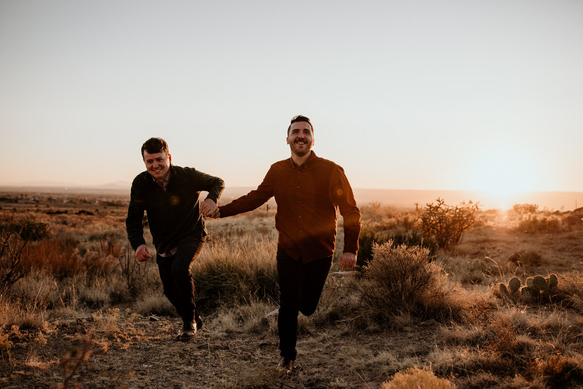 two men holding hands and running in the desert
