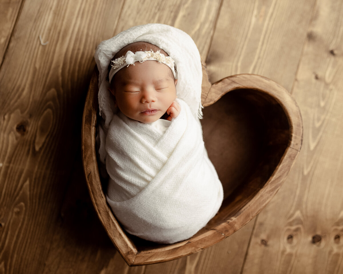 baby girl sleeping in a heart prop during newborn photoshoot