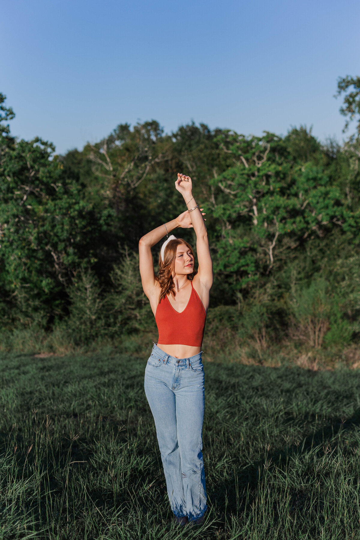 Red headed senior woman stands in a field with her arms gracefully above her head