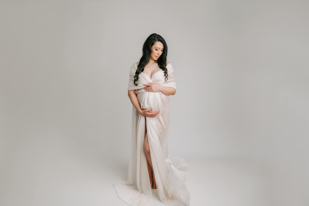 maternity portrait of pregnant woman wearing white silk on white backdrop