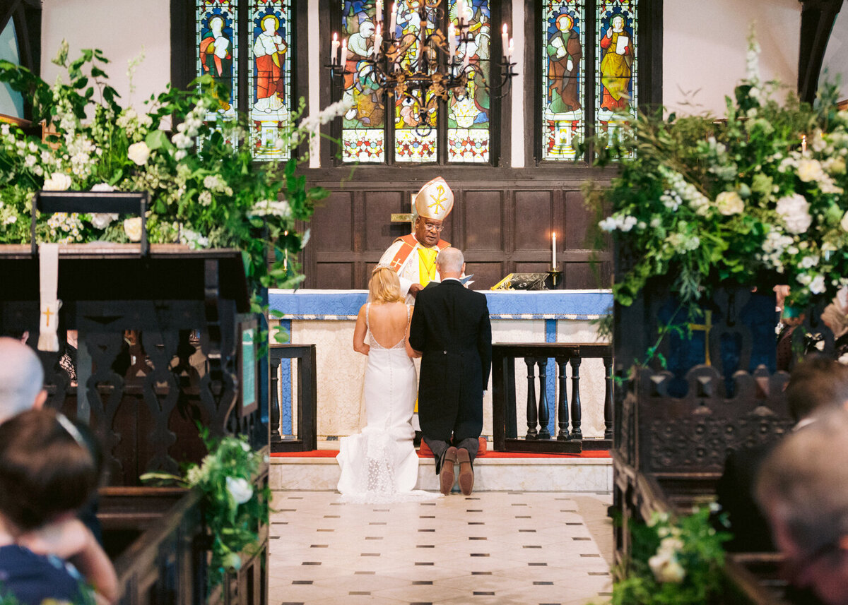 bride and groom kneels in front at the altar in front of the vicar