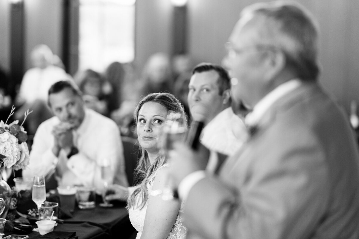 Bride looks on as her dad gives a speech.