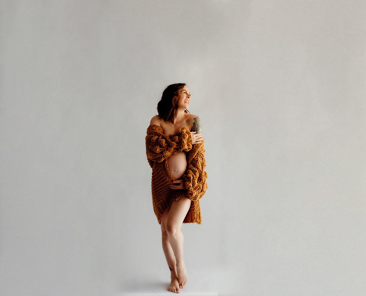 pregnant mom stands in white studio with white walls and background with bare belly showing