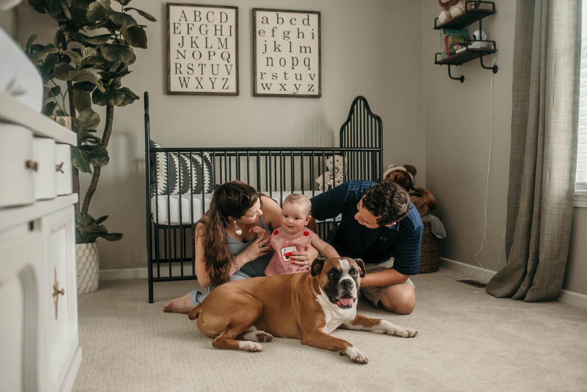 Mom, dad, dog, and baby sit in front of a crib