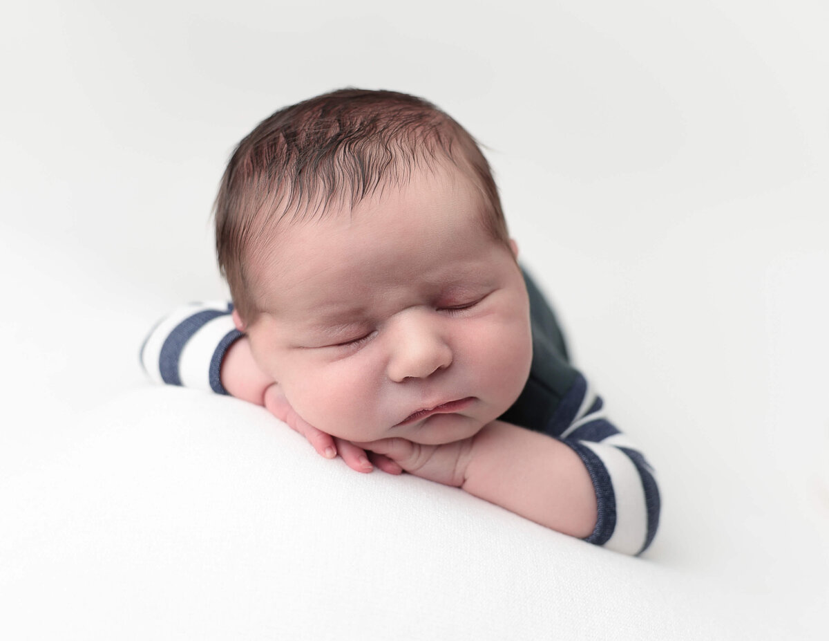 Baby boy posed withhead on hands at our Rochester, Ny studio.