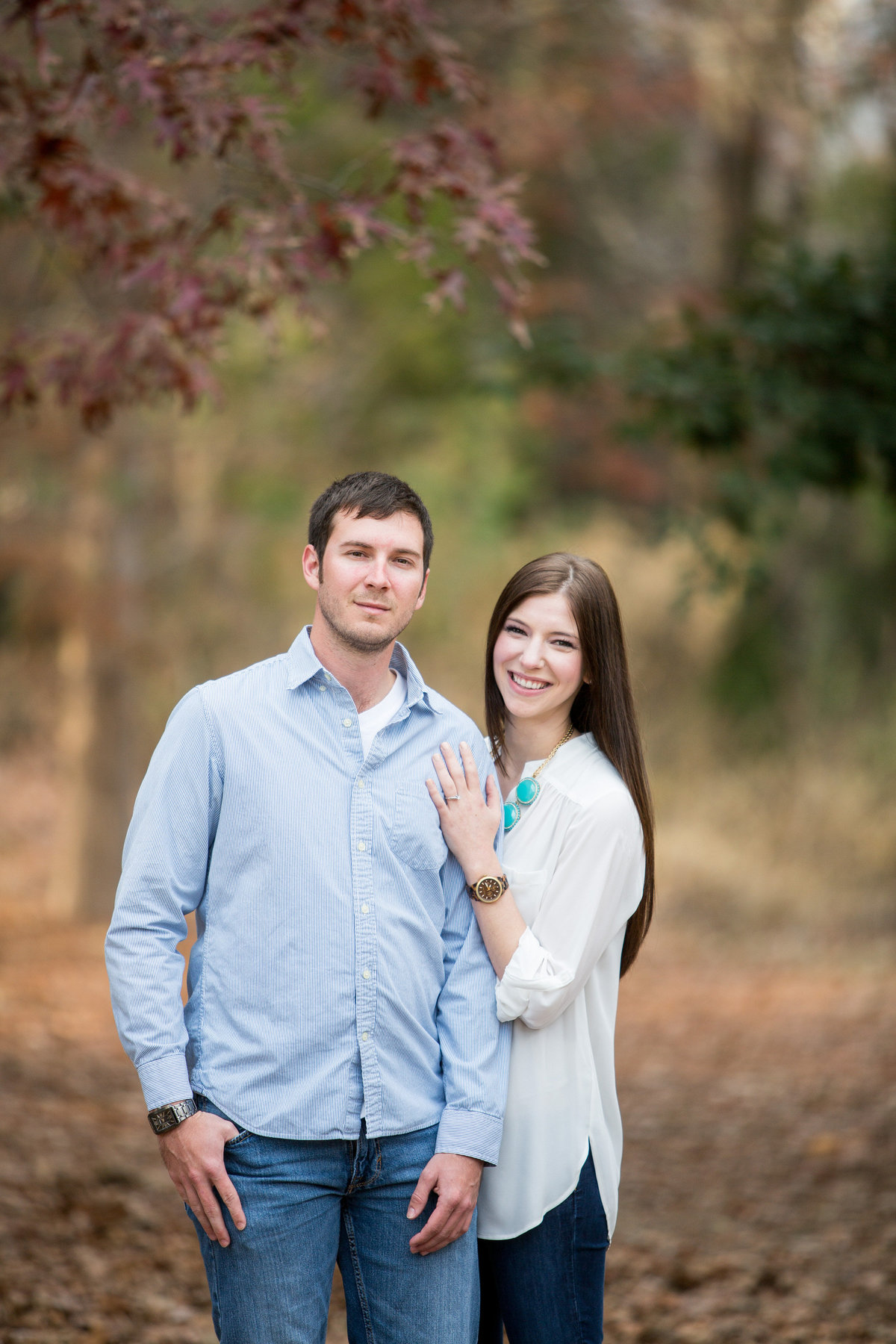 Engagement session of couple standing in clearing covered in leaves during the fall.
