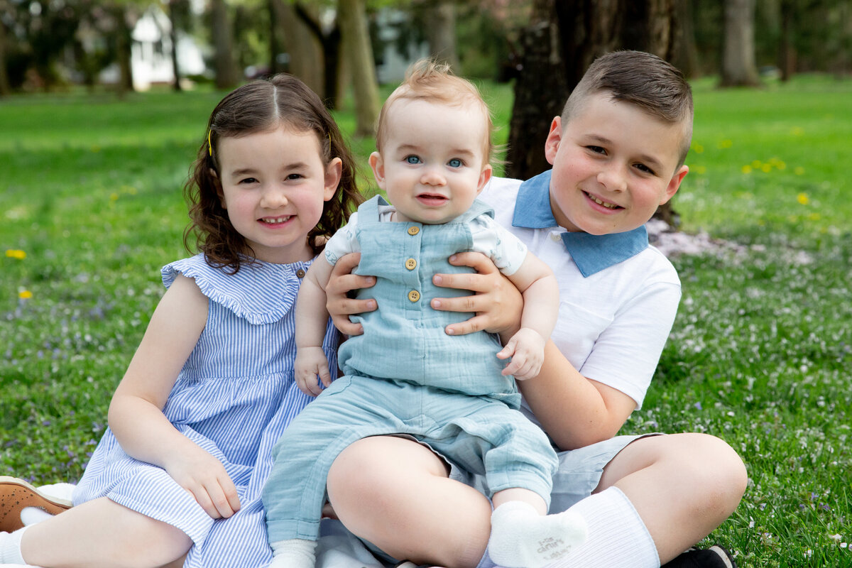 Three siblings in pastel outfits sit together on a blue blanket in a spring mini-session Rockland County mini-session photographer Milestone Images